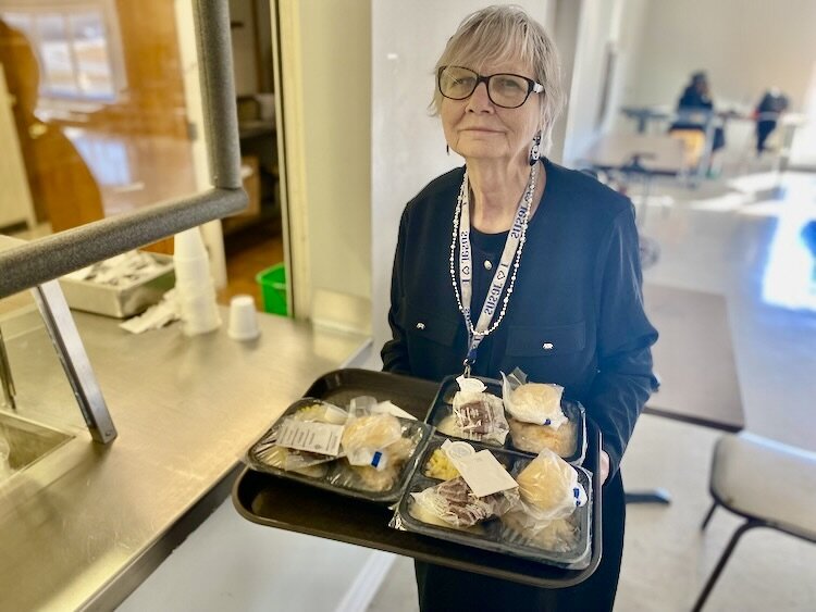 Congregate site volunteer Mary Malise delivers meals to a waiting table of seniors.